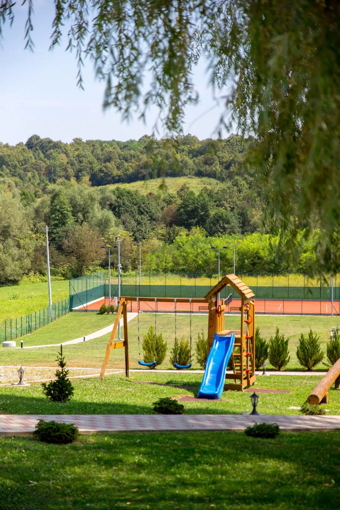 Children's playground with a slide, tennis court behind