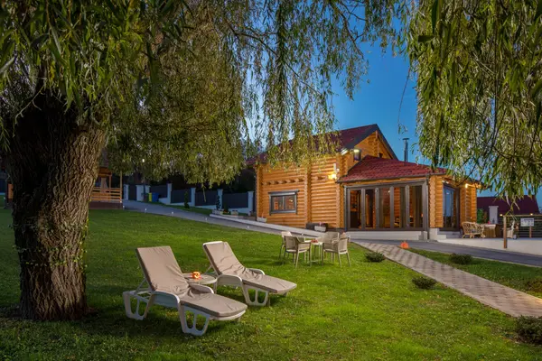 Ležaljke u hladu vrbe, u pozadini drvena kuća