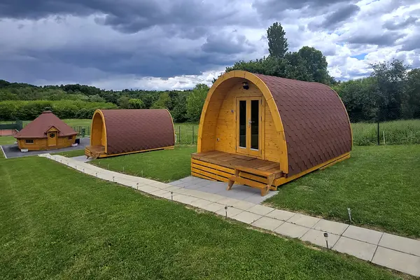Two wooden glamping cabins on the lawn, with the barbecue hut behind